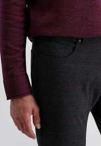Bordeaux trui met een textuurafwerking, gecombineerd met donker geruite broek met dunne rode lijnen, gedetailleerde zakken en een knoopsluiting.