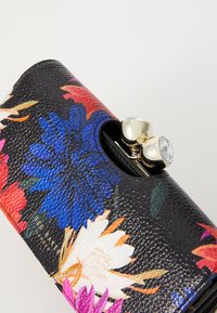 Lompakko-kotelo, jossa on kukkakuosi mustassa texuroidussa nahassa sinisten, vaaleanpunaisten ja valkoisten kukkien kanssa. Varustettu kultaisella kiinnityksellä, jossa on kaksi kirkasta koristekiveä.