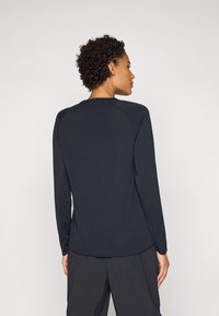 Maglietta nera a maniche lunghe realizzata in tessuto textured, con scollatura a girocollo e maniche raglan, orlo dritto e cuciture minime.
