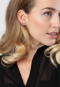 Gouden oorbellen met een klein hoopontwerp en een stud met een heldere edelsteen. Draagt een delicate gouden harthanger ketting.