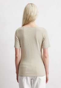 Camiseta de manga corta beige, hecha de una tela ligera con una textura suave, que presenta un escote redondo y una silueta ajustada.