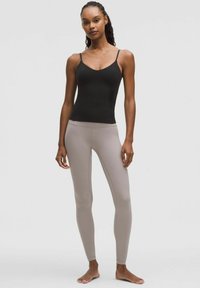 Black fitted tank top with thin straps, paired with light beige high-waisted leggings, both made of smooth, stretchy fabric.