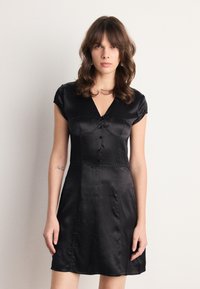 Robe en satin noir avec un décolleté en V, de courtes manches à capuchon et des détails en boutons sur le devant. Texture lisse et corsage ajusté menant à une jupe évasée.