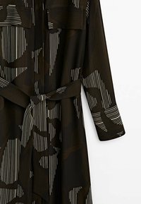 Robe noire à manches longues avec une bande verticale blanche et des motifs abstraits, avec des poches poitrine et une ceinture en tissu assortie nouée à la taille.