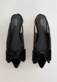 Melnas samta slingback kurpes ar norādītām pirkstiem un dekoratīvām loku dekorācijām priekšā. Gluda tekstūra, mīkstinātas ieliktņi un zīmola odere.