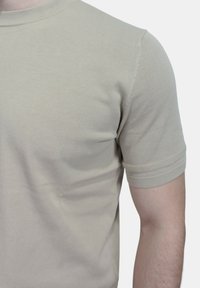 T-shirt beige a maniche corte realizzato in morbido cotone, con una vestibilità aderente, collo rotondo e cuciture rifinite con cura. Texture liscia con dettagli minimi.