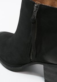 Bottine en daim noir avec fermeture éclair latérale et languette, dotée d'un talon carré et d'une doublure intérieure marron.