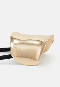 Gold-colored accessory with a smooth, rounded shape and reflective surface, attached to a black elastic cord.