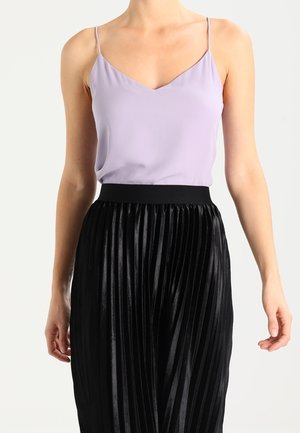 Lawendowa, bezrękawnikowa bluzka z dekoltem w serek w połączeniu z czarną plisowaną spódnicą z elastycznym pasem i błyszczącą fakturą.