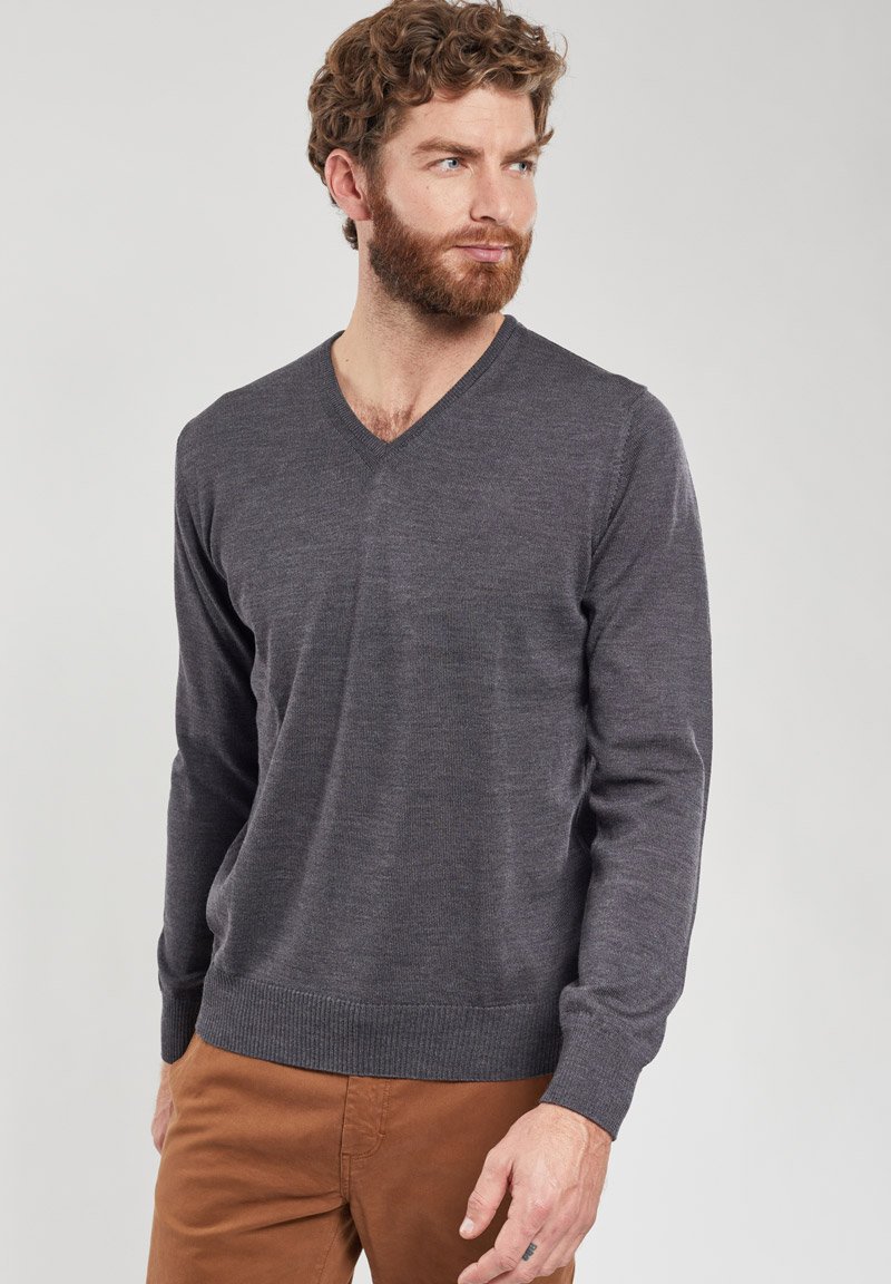 Pull gris en V en un matériau tricoté doux, avec des manches longues et un ourlet côtelé, associé à un chino marron. Fond neutre.