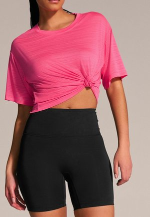 Rosa kortärmad träningstop med en knuten detalj fram, matchad med högmidjade svarta shorts. Slätt, lätt tyg.