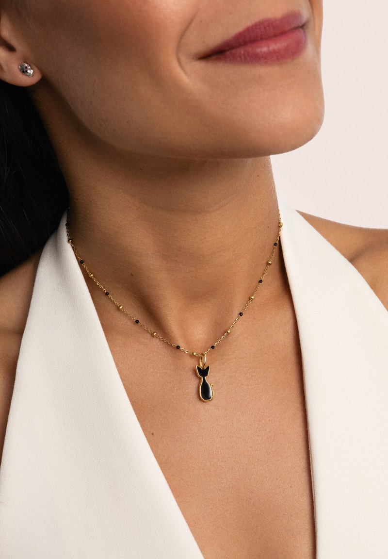 Collar de oro con un colgante negro en forma de gato con cola. La cadena es delicada y tiene pequeñas cuentas negras intercaladas.