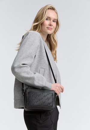 Schwarze Leder-Umhängetasche mit eingeprägtem Logo, rechteckige Form, silberne Hardware, kombiniert mit einer grauen Bomberjacke und schwarzen Hosen.