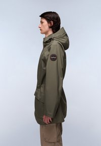Olivgrüne wasserdichte Jacke mit Kapuze, Kordelzug in der Taille und einem runden Patch auf dem linken Ärmel. Glatte Textur und funktionales Design.