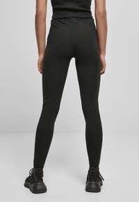 Zwarte legging van rekbaar materiaal met een hoge taille en geschulpte zoom. Strak ontwerp dat tot de enkels reikt. Gemaakt om te dragen met zwarte enkellaarzen.