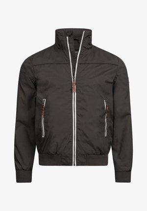 Dunkelgraue Zip-Jacke mit hohem Kragen, zwei Fronttaschen und kontrastierenden weißen Reißverschlüssen, kombiniert mit hellgrauen Hosen und schwarzen Sneakers.