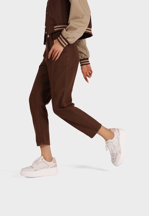 Pantaloni di velluto a coste marroni abbinati a una giacca bomber color block marrone e beige e sneakers con piattaforma bianche con accenti pastello.