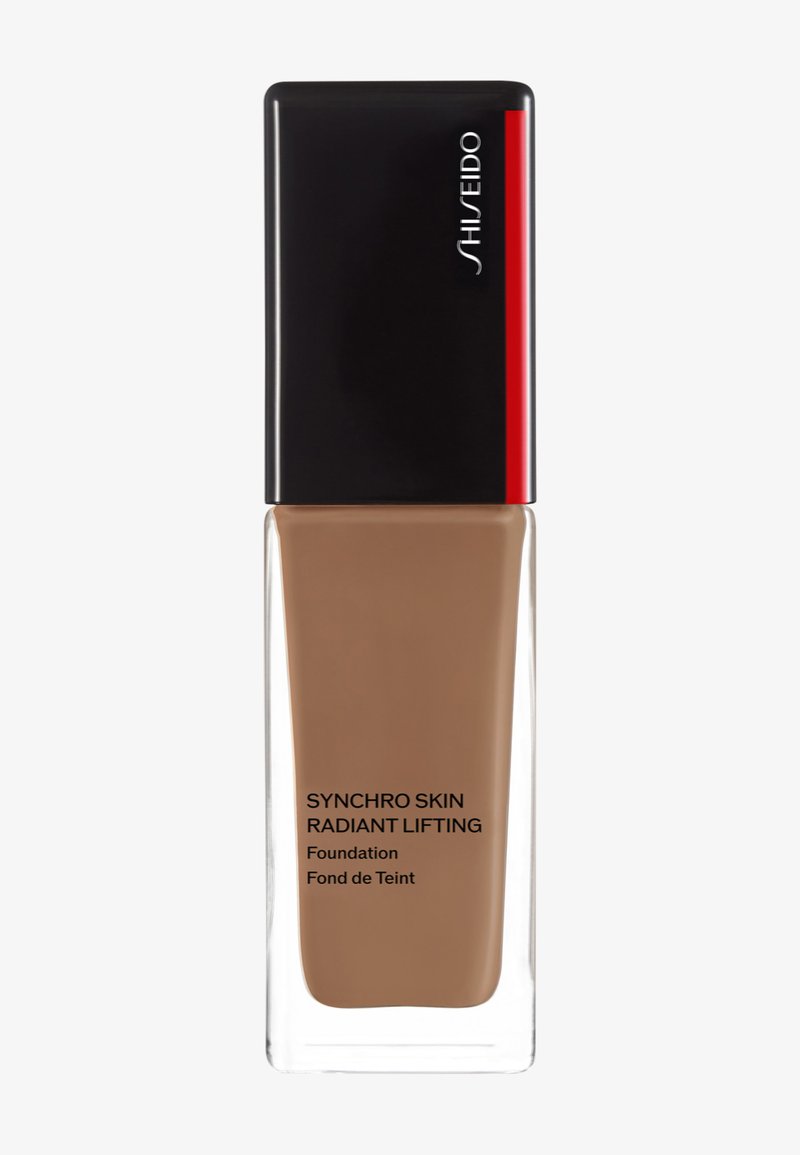 Shiseido Synchro Skin Radiant Lifting foundation i en klar glassflaske med et svart og rødt lokk; medium brun væske inni.