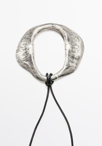 Metallic silver necklace with a textured, organic-shaped pendant and a black leather cord. Pendant features an irregular oval opening.