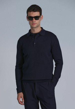 Dunkelblaues, geripptes Langarm-Polo mit Kragen und drei Knöpfen, kombiniert mit passenden dunklen Hosen. Glatte Textur, figurbetontes Design.