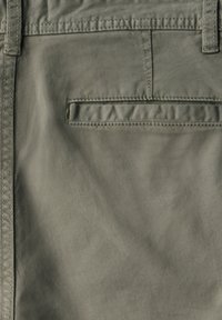 Khaki kalhoty vyrobené z lehkého materiálu, se zadní kapsou s obdélníkovým klopou. Povrch má hladkou, mírně lesklou texturu.