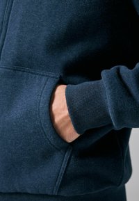 Tmavě námořnická mikina s klokankou a žebrovanými zápěstími. Vyrobena z měkké tkaniny s texturovaným povrchem, který zdůrazňuje její pohodlí.
