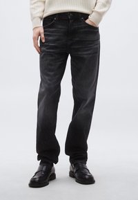 Fekete farmernadrág laza szabással, klasszikus ötpocketes kialakítással és enyhe kifakulással, fekete mokaszinokkal párosítva.