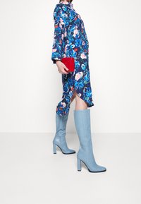 Abito lungo a maniche lunghe floreale con fiori blu, rosa e bianchi; pochette rossa; stivali al ginocchio in stampa serpente blu chiaro con tacco a blocco.