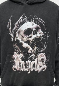 Ανθρώπινο κρανίο με σκελετικό χέρι και κύκλο από αλυσίδα με αγκάθια σε μαύρο φούτερ, με στιλιζαρισμένο κείμενο από κάτω.