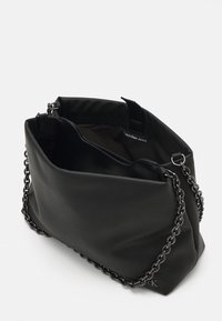 Black nylon handbag with a chain strap, featuring a soft, structured design and an inner pocket. Calvin Klein Jeans logo visible inside.