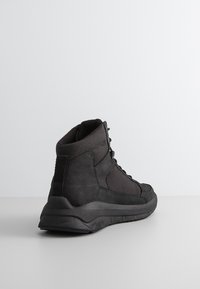 Czarne sneakersy typu high-top mają teksturowaną tkaninę w górnej części, wyściełane wsparcie kostki, wzmocnioną piętę oraz grubą gumową podeszwę z geometrycznym wzorem trakcji.