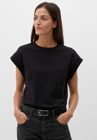 Czarny, krótki t-shirt bawełniany z okrągłym dekoltem i podwiniętymi rękawami, w połączeniu z ciemnoniebieskimi dżinsami i czarnym paskiem.