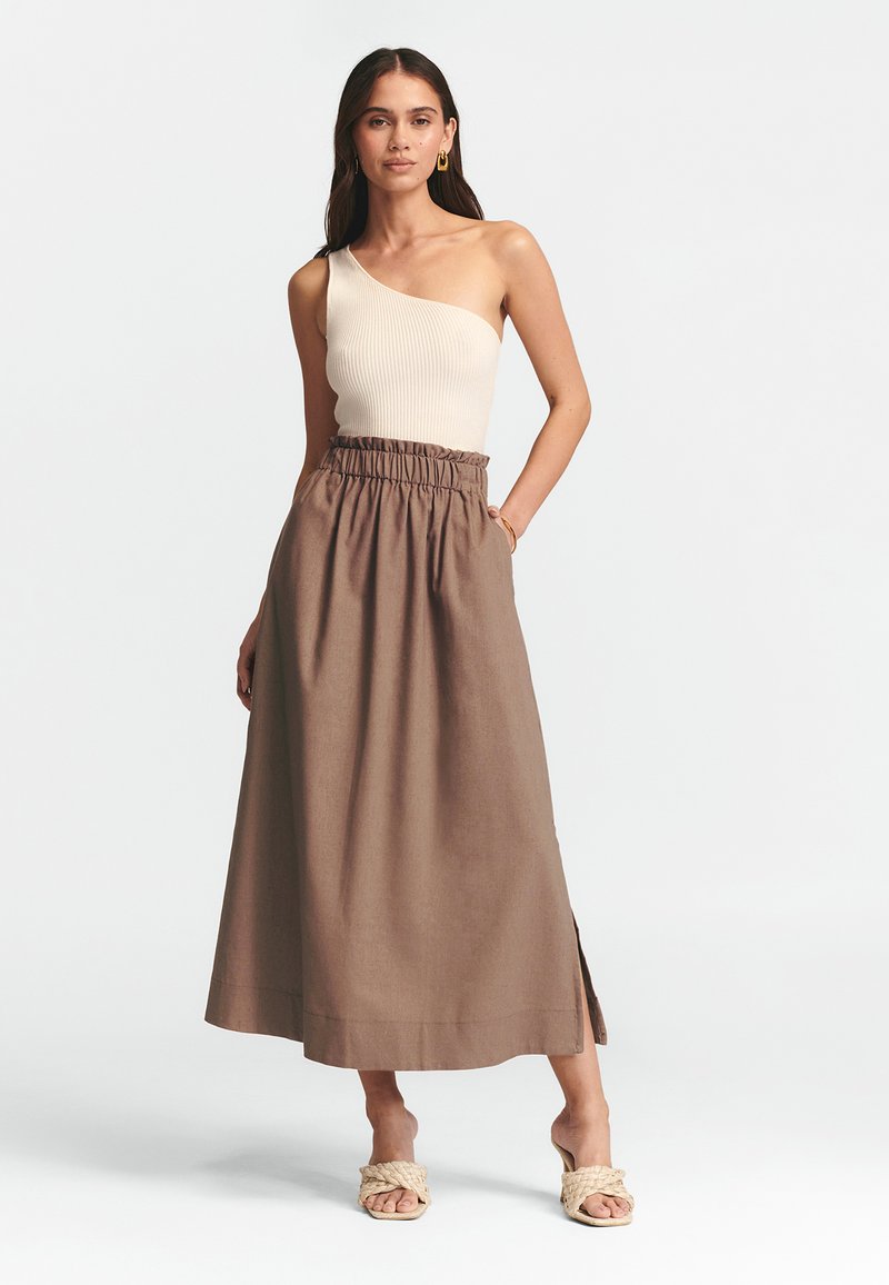 Beige geripptes Top mit einem Schulterträger, kombiniert mit einem braunen Maxirock mit elastischem Bund und seitlichem Schlitz. Sandalen mit geflochtenen Riemen.