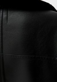 Czarna skórzana kurtka o teksturowanej powierzchni, z widocznymi szwami i futrzanym kołnierzem. Projekt podkreśla gładkie, wypolerowane wykończenie.