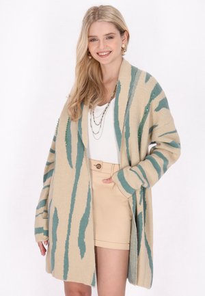 Beige cardigan met teal tijgerstrepen, gemaakt van zacht gebreid materiaal. Heeft een open voorkant, lange mouwen en zakken aan de zijkanten.