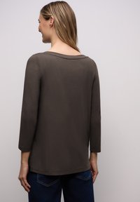 Dunkelgraues Langarmshirt mit weitem Ausschnitt, glatter Textur und lockerem Sitz, kombiniert mit blauen Jeans aus Denim.