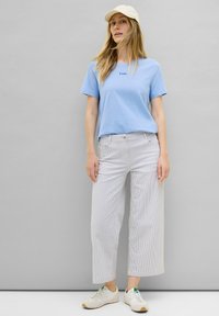 Himmelblaues T-Shirt mit kurzen Ärmeln und kleinem Logo, kombiniert mit weiten, hell gestreiften Hosen und weißen Sneakers mit grünen Akzenten.