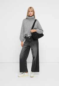 Grå turtleneck genser, vide sorte jeans med kontrastpanel, svart håndveske og hvite sneakers med gule detaljer.