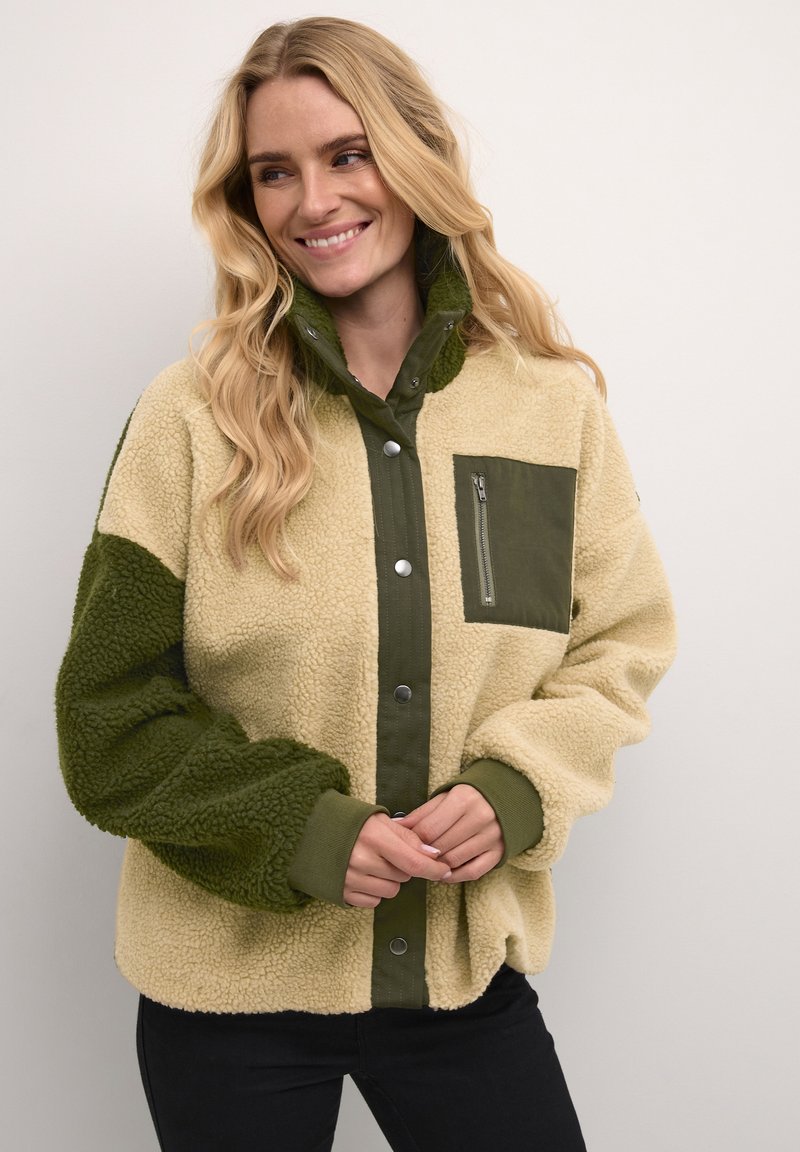 Giacca in fleece beige e verde, con chiusura a bottoni a pressione, tasca con zip sul petto e polsini a coste. Tessuto morbido e testurizzato.