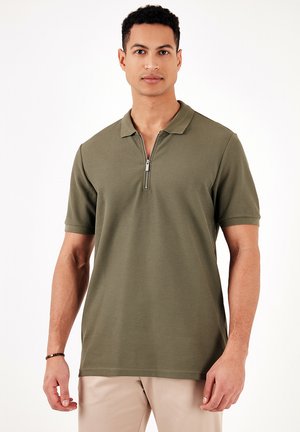 Polo verde oliva con maniche corte, colletto a mezza zip, tessuto texturizzato e orlo piatto. Adatto per un abbigliamento casual.