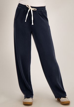 Marineblauwe casual sweatpants met witte trekkoorden, elastische tailleband, zijzakken, gedragen met witte sneakers en een wit topje.
