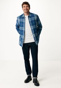 Camicia a quadri blu sopra una maglietta bianca, abbinata a jeans scuri e stivali neri. Presenta bottoni, maniche lunghe e una vestibilità comoda.