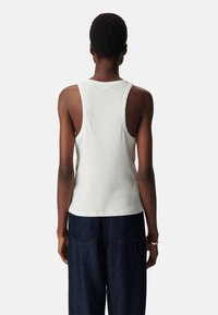 Witte geribbelde tanktop met brede schouderbanden, aansluitende pasvorm en een gladde textuur. Draagt een combinatie met donkerblauwe high-waisted broek.