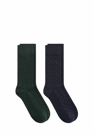 Deux paires de longues chaussettes, une unie vert foncé avec une texture côtelée, l'autre bleu marine foncé avec de petits pois verts.