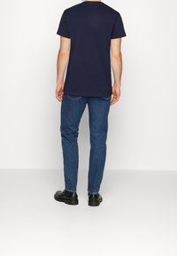 Camiseta de algodón de manga corta en azul marino combinada con jeans de mezclilla oscuros y botas negras hasta el tobillo, vista desde la parte de atrás, mostrando un atuendo casual.