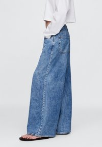 Ženske široke jeans hlače svetlo modre barve z visokim pasom, ravnim krojem in klasičnim dizajnom zadnjih žepov. Mehka, teksturirana tkanina.