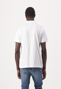 Witte poloshirt met korte mouwen, een geribbelde kraag, een gladde textuur en een rechte zoom, gedragen met blauwe spijkerbroeken.