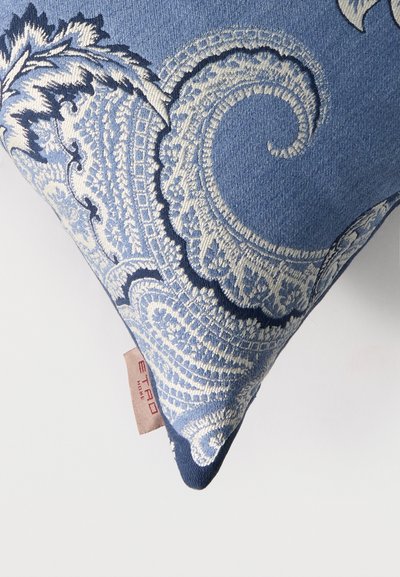 Coussin décoratif bleu avec une broderie blanche complexe de style cachemire et une petite étiquette beige avec l'inscription « ETRO HOME » sur fond blanc.