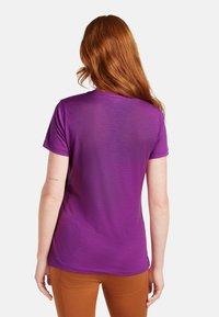 Camiseta morada de manga corta con una tela suave, diseño de cuello redondo y un corte relajado, combinada con pantalones marrones.