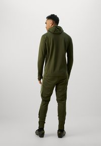 Tuta verde oliva composto da giacca con cappuccio e pantaloni affusolati con strisce laterali. Realizzato in tessuto morbido, progettato per comfort e mobilità.